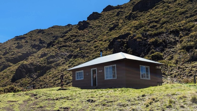 A hiker standing next to a Kapalaoa Cabin at the foot of a volcanic ridge at Haleakalā National Park, in Maui, Hawaii.