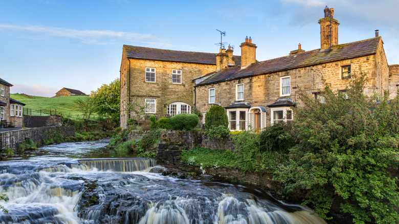 Old English brick buildings in Hawes on the banks of a small rushing river with little rapids and vibrant green vegetation on its side