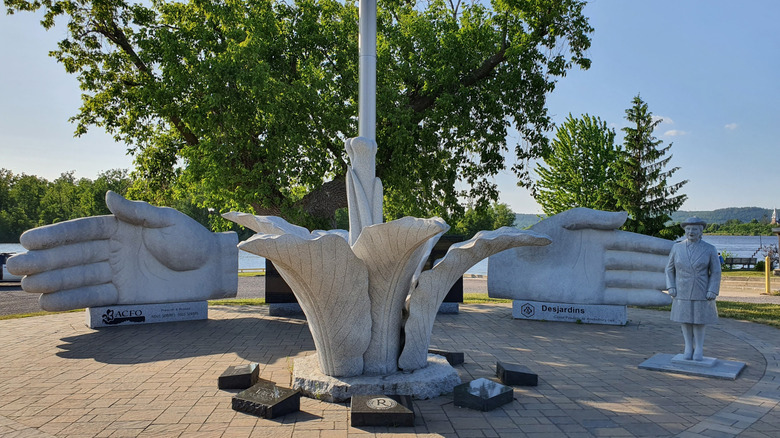 Sculptures of two hands cupping a lily flower with tree-lined river background