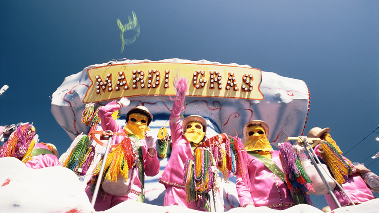 People in costumes on a Mardi Gras float throwing plastic beads into the crowd