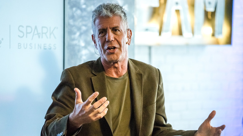 Anthony Bourdain in a green shirt and jacket speaking