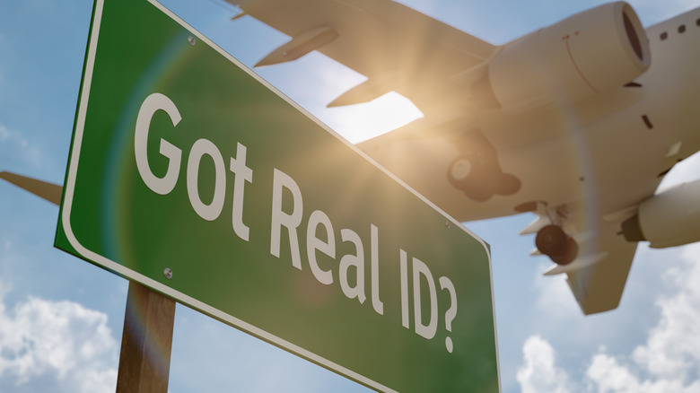A REAL ID sign at the airport with a plane landing overhead