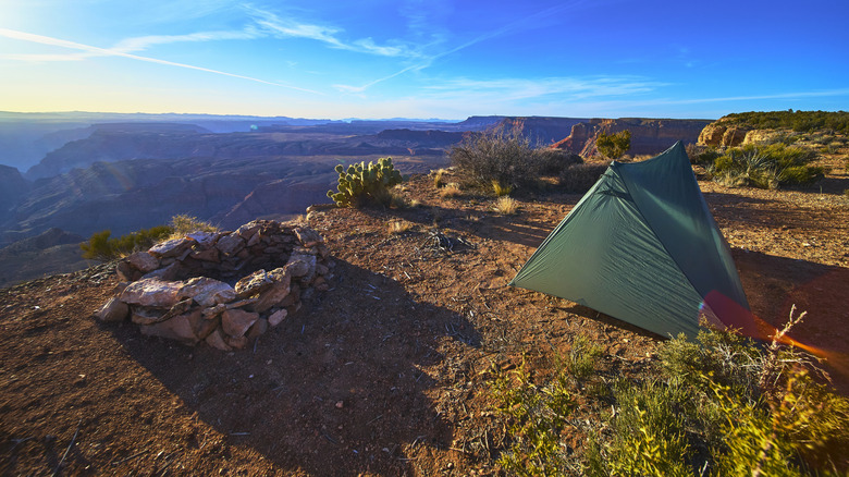 Small, green tent pitched on a dirt lot in front of the Grand Canyon, Arizona