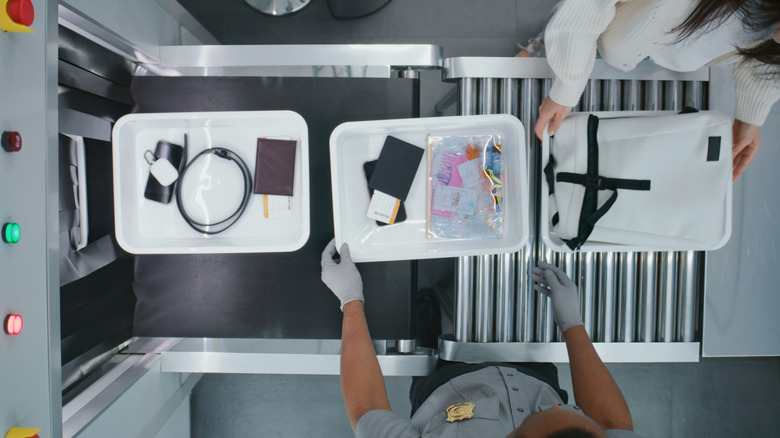 Items and bags in various trays making their way along a conveyor belt and into a scanning device at an airport