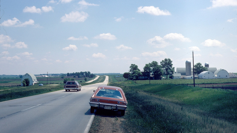 1970s cars travel down a Midwest road