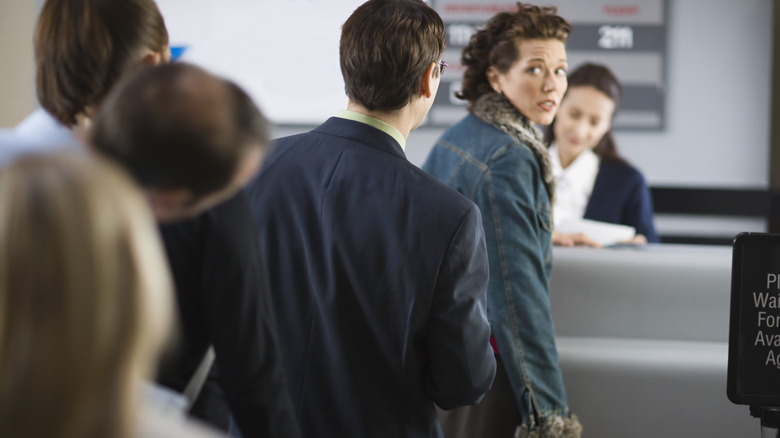 Worried airline passenger looking back at a crowd of people while infront of an airline agent