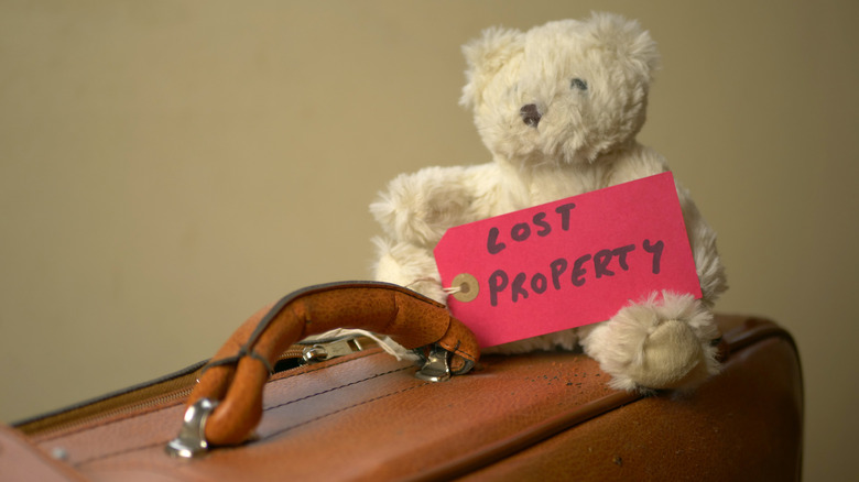 Close-up image of a small teddy bear on top of a vintage leather suitcase, with a red tag labeled "Lost Property" on it.