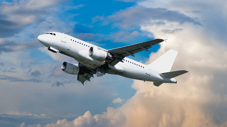 A commercial plane soars through the cloud-filled sky around sunset