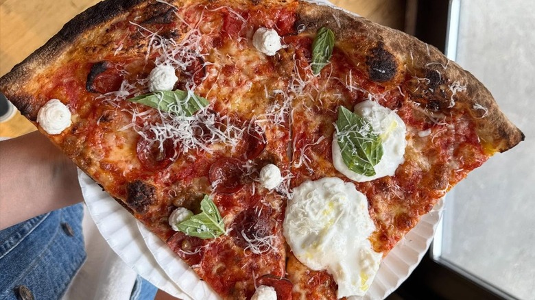 The iconic Burrata and award-winning New Yorker New York-style pizza slices at L'Industrie, held on a paper plate