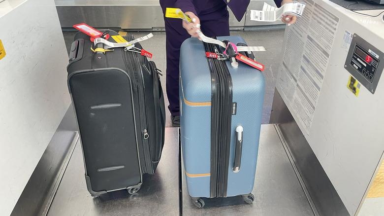 Two suitcases on a scale with an attendant putting a luggage tag on it