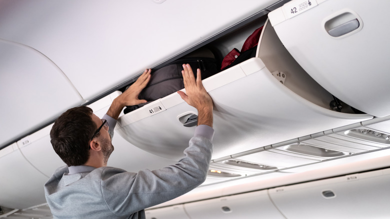 Person putting their bag in overhead bin