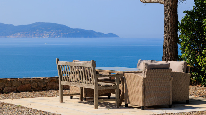 A garden seating area with loungers overlooking blue sea and mountains in the distance.