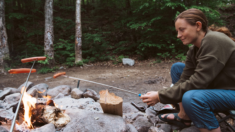Female backpacker cooking hotdogs over a fire in the wilderness