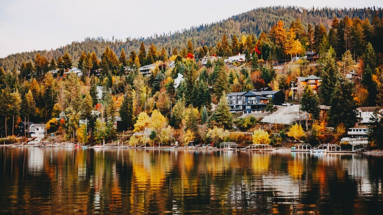 Fall colors at Hayden Lake, with colorful trees reflecting in the water around mountain-side homes