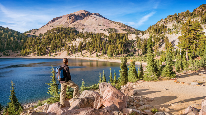 A hiker looking at view in Lassen Volcanic National Park on a sunny day, with Lake Helen and Lassen Peak in the background