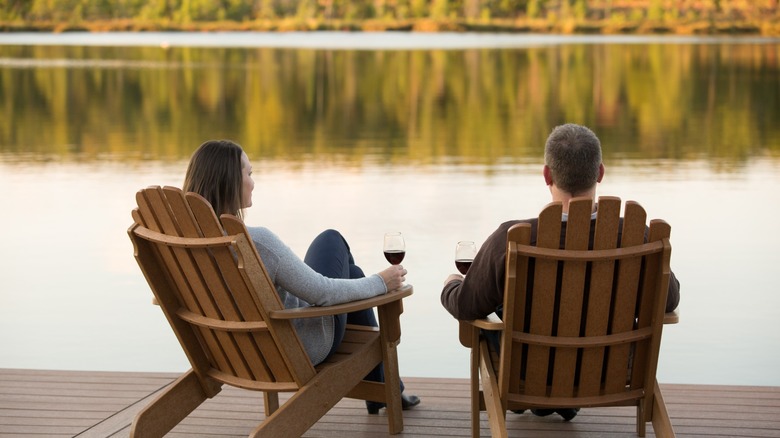 Couple sitting on lake at The Lodge at Woodloch drinking wine in Adirondack chairs