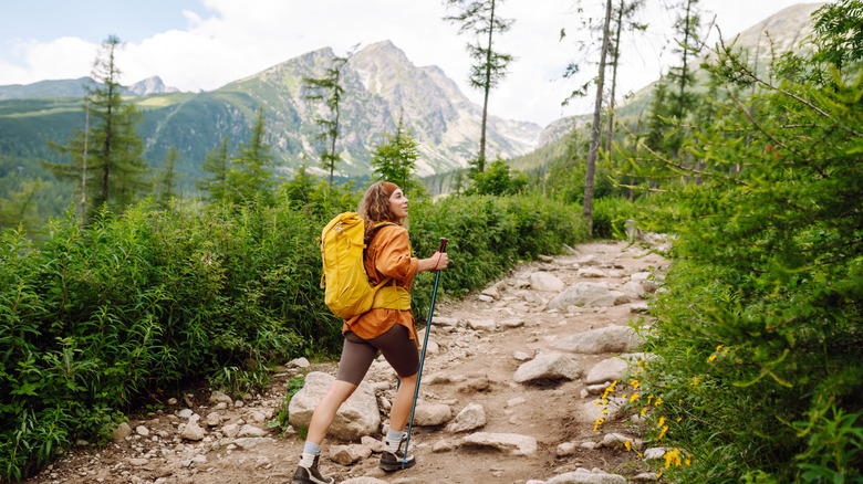 Female hiker with yellow hiking backpack climbing rocky path