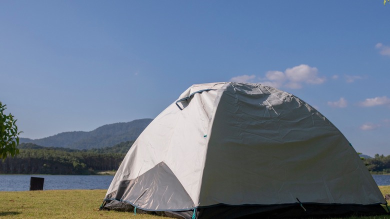 A tent pitched by blue water with mountains in the background