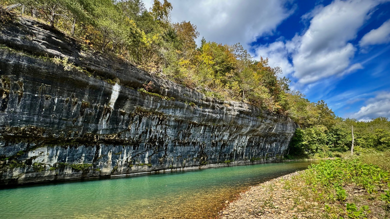 Sheer limestone wall against turquoise Buffalo River and blue sky with clouds Ponca Arkansas