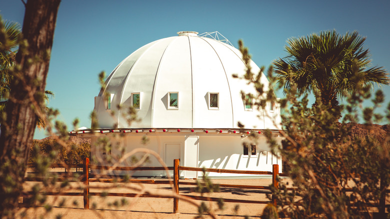 The Integratron, a sixteen-sided white dome can be seen behind a wooden fence, beneath a blue sky
