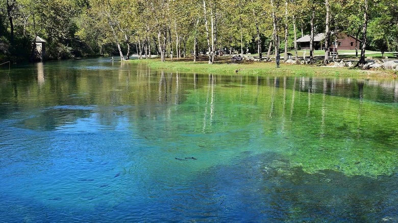 A lake with blue and green water at Bennett Spring State Park, with trees and a cabin in the background
