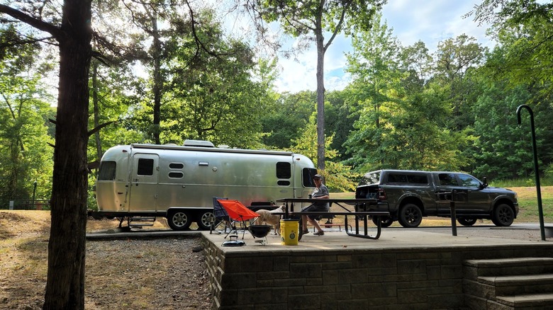 A silver trailer parked on a stone patio in a heavily wooded campground at Lake Fort Smith State Park, Arkansas