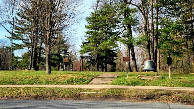 Small park in Eagles Mere, Pennsylvania with a bell, trees, and small gazebo.