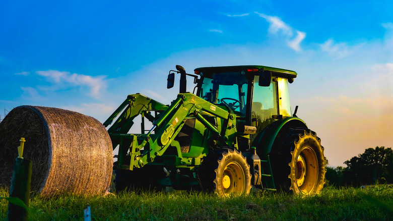 A tractor with hay bale on farm with blue and yellow sky, Riner, Virginia