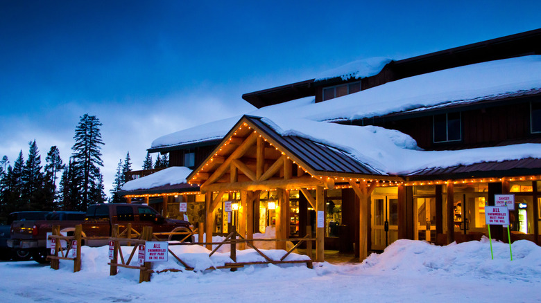 Togwotee Mountain Lodge in the evening with warm lights illuminating the cabin-like entrance with trees and snow surrounding