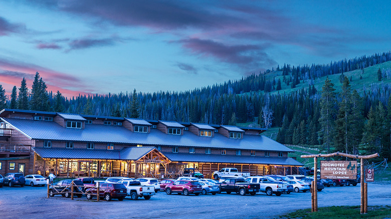 Full view of Togwotee Mountain Lodge with cars parked out front and trees on a mountainside in the background