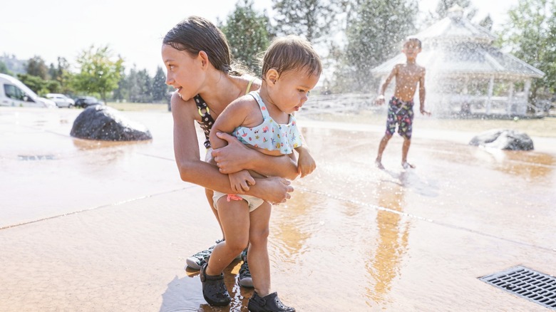 Young girl holds a toddler at a spray ground
