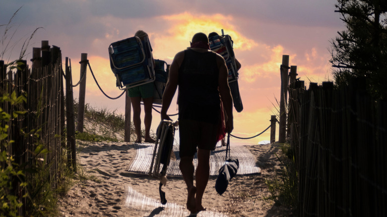 A group of people carry beach chairs to the beach