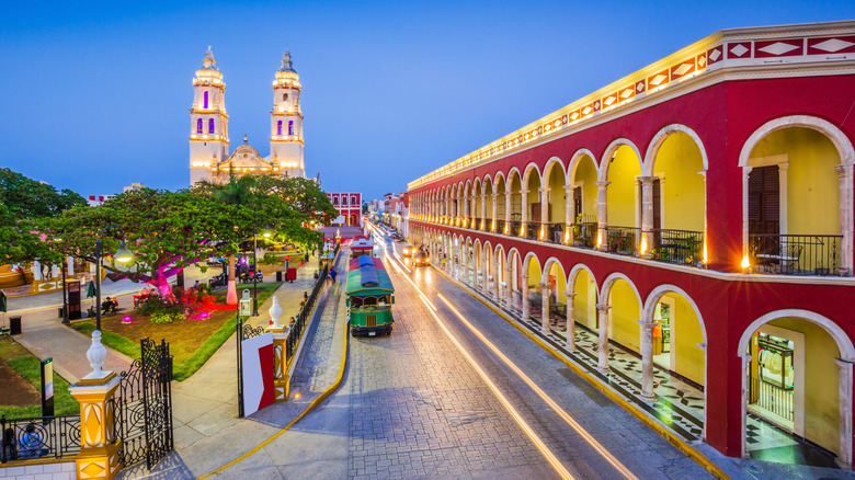 A view of central Campeche in the early evening, with lit-up cathedral, colonial buildings, and cobblestone streets lined with vintage trams