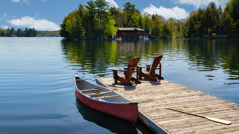 Adirondack chairs and canoe by a dock facing a lake in Muskoka