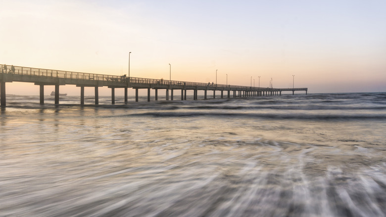 A long exposure photo of waves coming in to the shore on Mustang Island, with a pier stretching towards the horizon