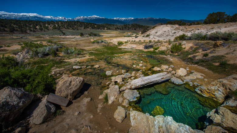 A turquoise mineral pool surrounded by rocks overlooks the Sierra Nevada Mountains at Travertine Hot Springs