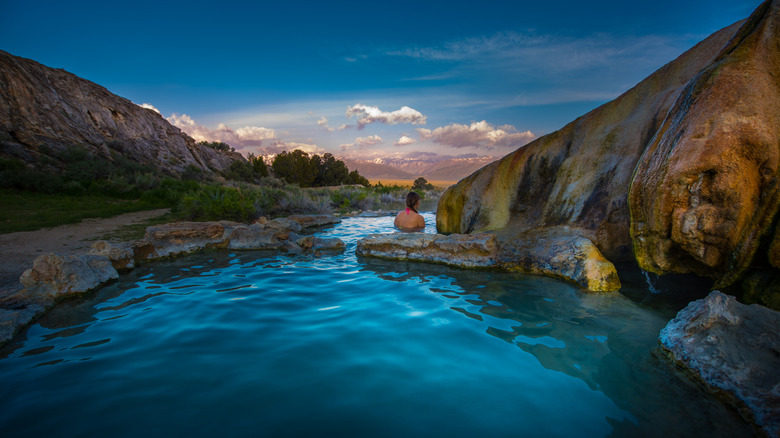 A woman in a pink bathing suit soaks in a mineral pool overlooking the Sierra Nevada Mountains at Travertine Hot Springs