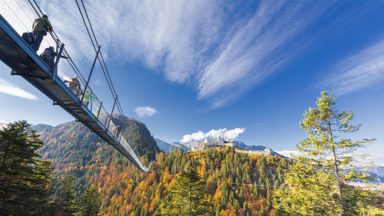 Tourists cross a steel suspension bridge in the Alps leading to the ruins of medieval Ehrenberg Castle