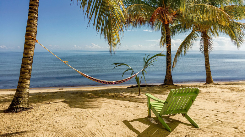 A green beach chair and a hammock set up on the beach in Hopkins, Belize