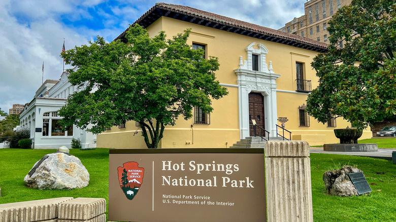 A sign for Hot Springs National Park and the yellow administrative building on Bathhouse Row in Hot Springs, Arkansas