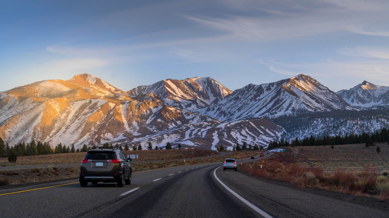 Cars driving towards a mountain range at sunset