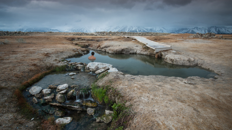 A man soaks in hot springs with snow-capped mountains in the distance in California