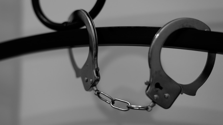 Close-up of a pair of handcuffs attached to black metal bed frame in front of white wall