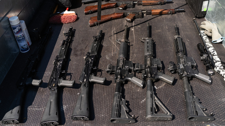 AK and AR-15 platform rifles alongside classic guns like a Thompson submachine gun, laid out inside a vehicle trailer.