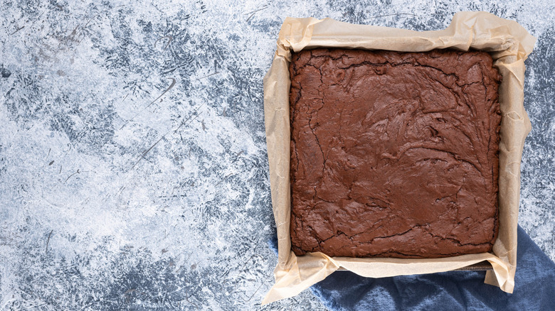 Parchment lined baking pan with fresh baked, dark chocolate espresso brownies, white and gray textured background.