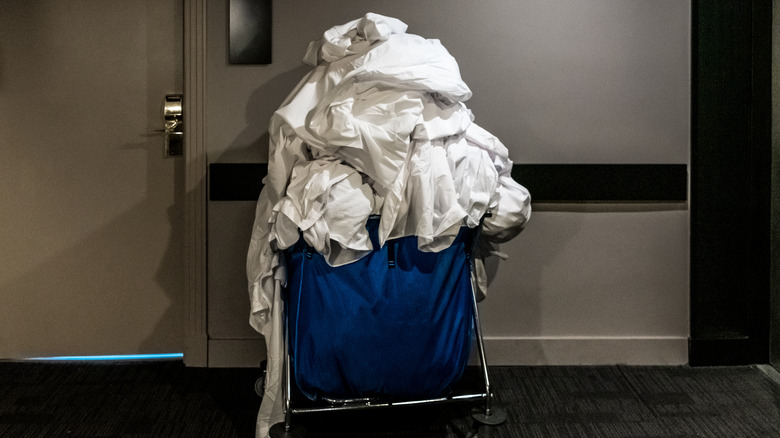 Blue trolley full of dirty white sheets and linens in a hotel hallway