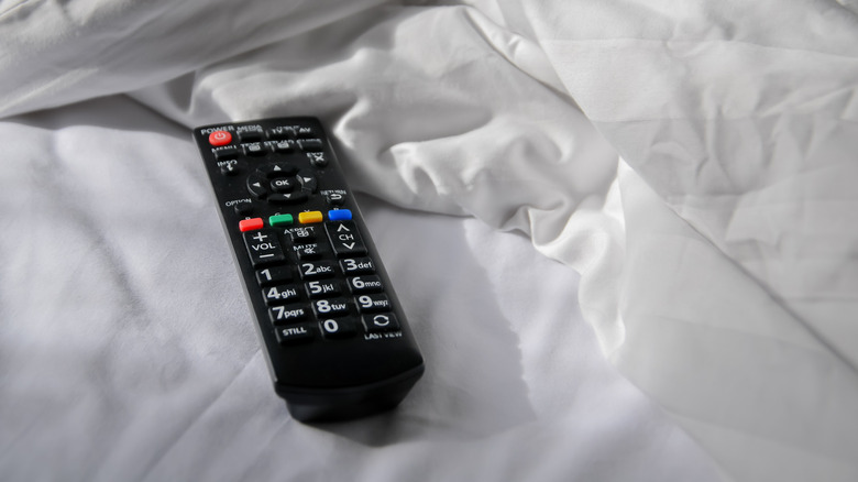 A black TV remote in a messy bed with white sheets.