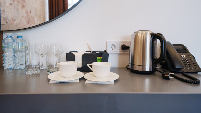 A kettle and cups on the side in a hotel room.