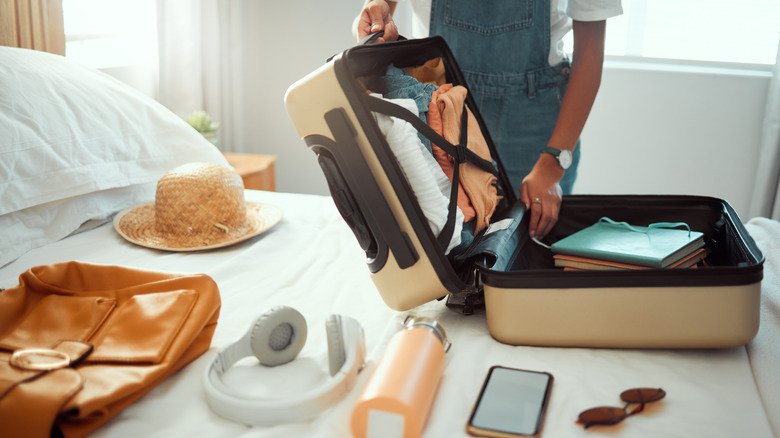 Woman un packing her suitcase on a hotel room bed.