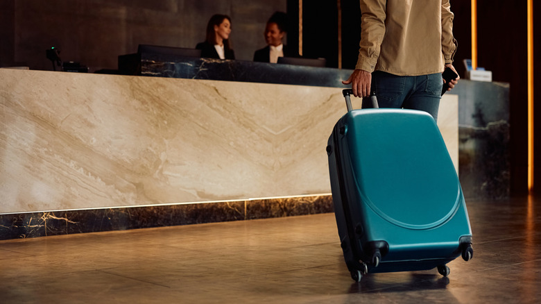 closeup of guest with suitcase approaching hotel front desk